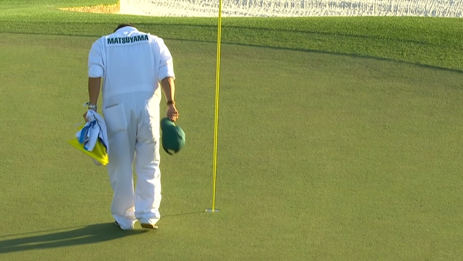 Matsuyama's caddie bows after placing the 18th hole pin